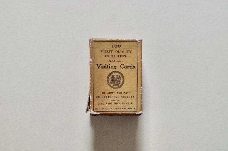Pode incluir: Uma caixa retangular de "Visiting Cards" bege com texto preto, incluindo "Finest Quality" e "De La Rue's". A caixa, ligeiramente desgastada, tamb&eacute;m mostra o nome "The Army and Navy Co-operative Society".