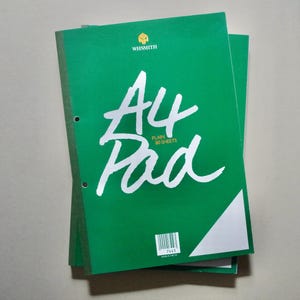 Może przedstawiać: Stos zielonych notatników A4. Okładka górnego notatnika zawiera napis "A4 Pad" w białym skrypcie, wraz z nazwą marki "WHSmith" i napisem "PLAIN 80 SHEETS". Notatniki mają trzy otwory do oprawy.