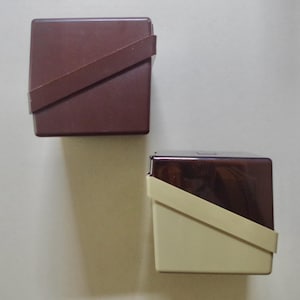 May include: Two square storage containers with diagonal bands across the front. The top container is solid dark brown. The bottom container features a dark brown top section and a cream-coloured bottom section, separated by a diagonal cream band.