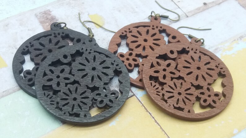Pode incluir: Dois pares de brincos de madeira com um design floral. Um par &eacute; castanho escuro, o outro &eacute; castanho claro. Os brincos s&atilde;o circulares com intrincados padr&otilde;es recortados de flores e folhas e t&ecirc;m ganchos de orelha cor de bronze.