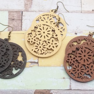 Pode incluir: Tr&ecirc;s pares de brincos de madeira com recortes florais. Um par &eacute; castanho escuro, um &eacute; bege claro e o outro &eacute; castanho m&eacute;dio. Cada brinco tem formato circular com intrincados desenhos florais e ganchos de orelha cor de bronze.
