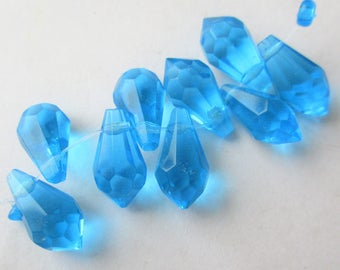 May include: A strand of light blue faceted teardrop glass beads. The beads are strung on a clear thread.