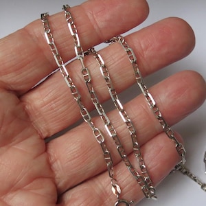 Peut inclure: Une chaîne de collier en métal argenté composée de maillons rectangulaires allongés avec une barre horizontale centrale dans chaque maillon. La chaîne comprend un fermoir à ressort circulaire à une extrémité, avec une finition polie et brillante.