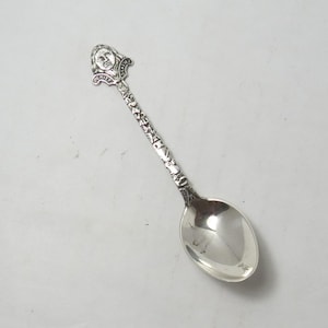 May include: A silver spoon with a detailed handle and bowl. The handle features a sculpted face and the words "CHIEF" and "SEATTLE". The spoon's stem is adorned with intricate patterns. The spoon is likely a souvenir or collectible item.