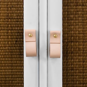 May include: White cabinet with two drawers and two doors. The drawers and doors have leather pulls with brass accents. The doors have a woven brown fabric panel.