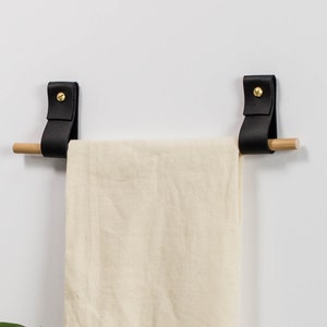 Two wall straps used with a wooden dowel to create a towel bar on which a tea towel is hung.