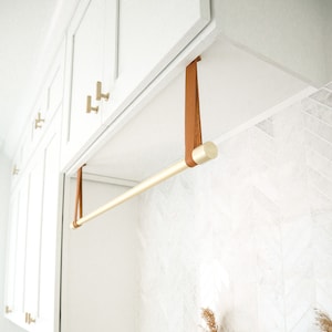 A laundry rack installed with Suspension Straps under a cabinet in a laundry room above a sink.