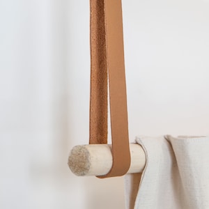 A closeup of a Leather Suspension Strap hanging a curtain with a wooden dowel.