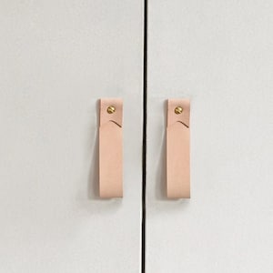 May include: Two light pink leather cabinet pulls with gold metal hardware.