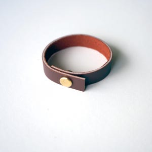 Warm mahogany full-grain leather loop with reddish undertones and a brass screw accent, displayed on white background.