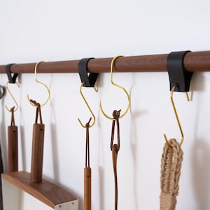 Metal Hooks & Leather Loops hanging from a wooden dowel suspended on the wall.