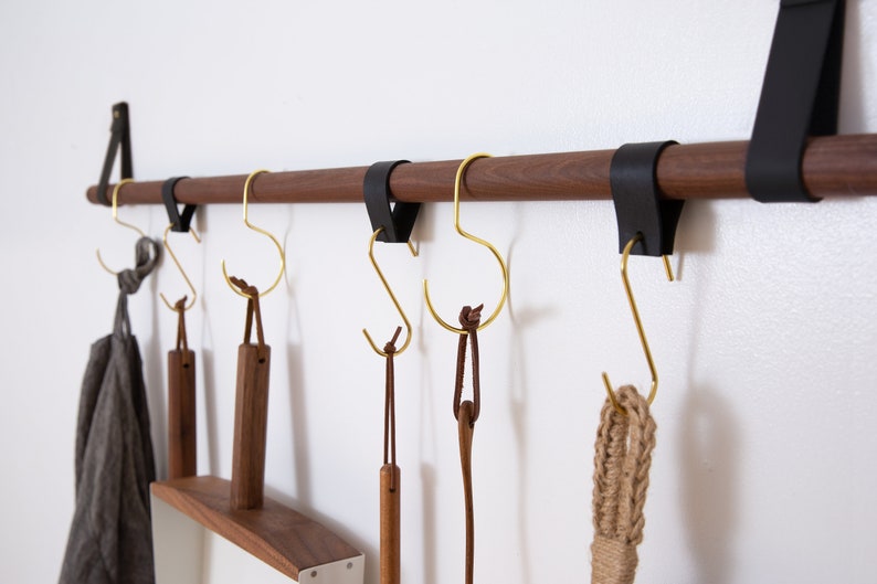 Metal Hooks & Leather Loops hanging from a wooden dowel suspended on the wall.