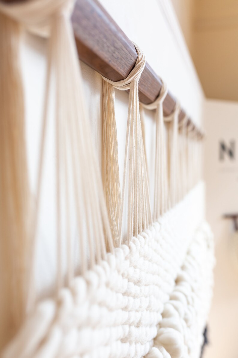 May include: A white macrame wall hanging with a wooden dowel at the top. The macrame is made with thick white yarn and has a textured, woven pattern.