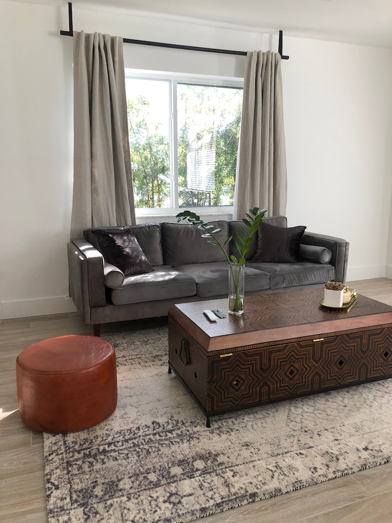 Curtains hang from Leather Suspension Straps in a living room window behind a sofa.