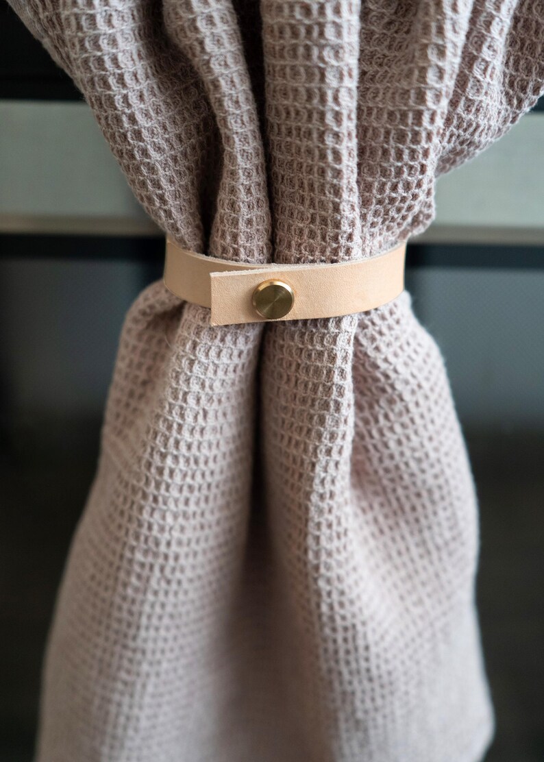 Neutral kitchen towel gathered with a natural veg-tan leather strap, handcrafted from vegetable-tanned full-grain leather using eco-friendly tanning processes. The brass screw closure and minimalist design reflect Keyaiira’s sustainable approach to modern home essentials.