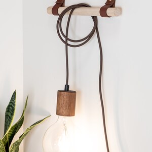 Two wall straps used with a wooden dowel to hang a light cord fixture.