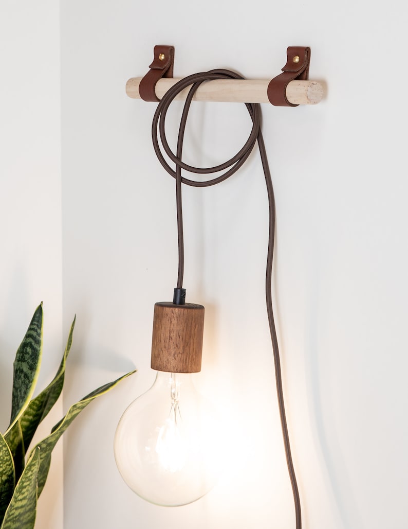 Two wall straps used with a wooden dowel to hang a light cord fixture.