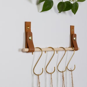 Two wall straps used with a wooden dowel to create a hanging rack on which measuring cups are hung with S Hooks.