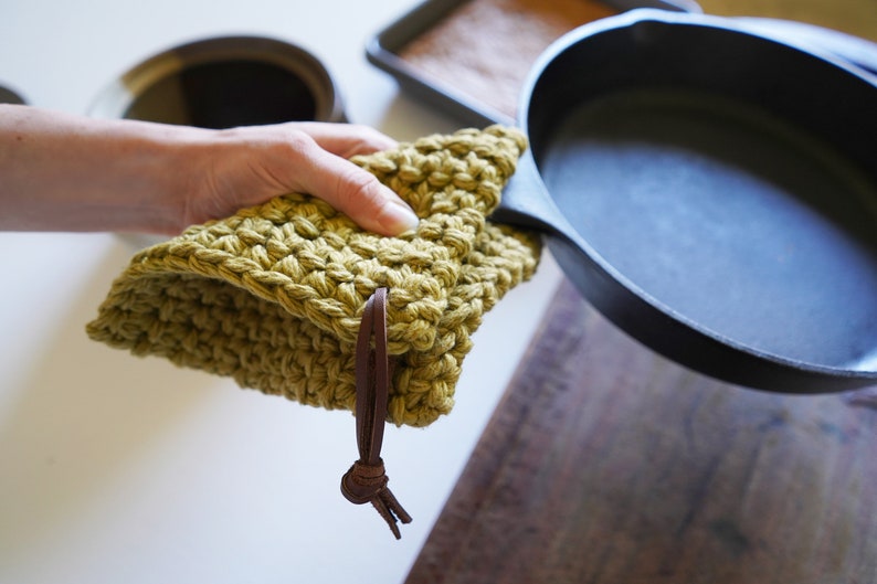Model holding cast iron pan covering the handle with a pot holder.