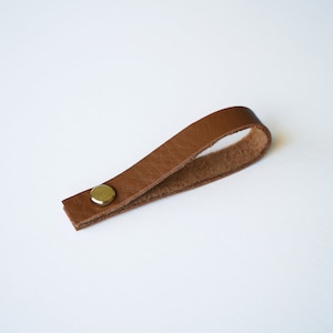May include: A brown leather loop with a brass button. The loop is designed to be used as a handle or a strap.