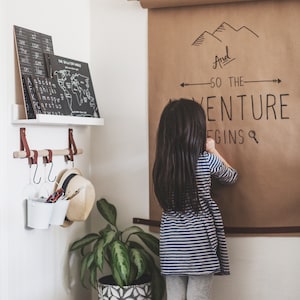 A child stands on the right of a hanging bar which holds two buckets of writing utensils hung by S Hooks.