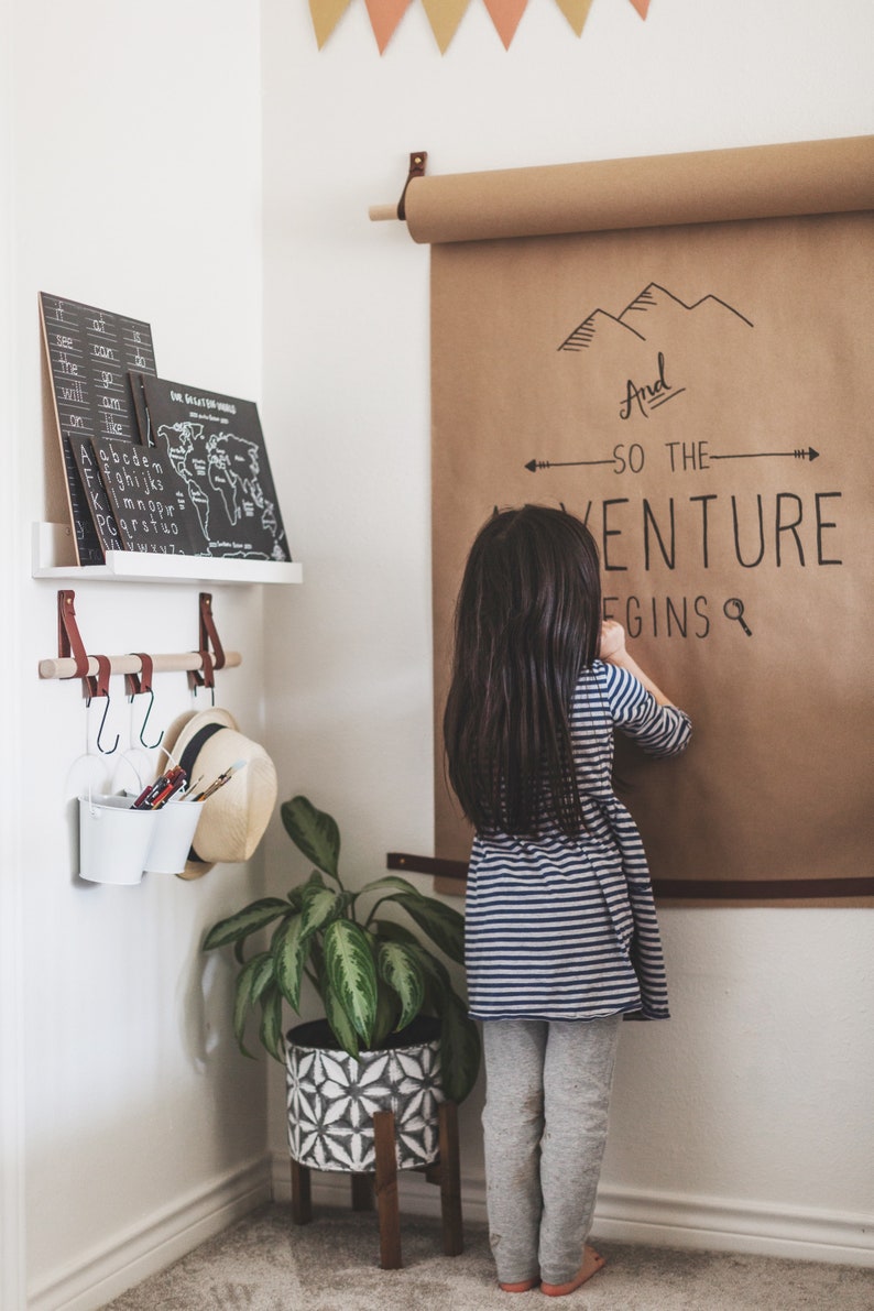 A child stands on the right of a hanging bar which holds two buckets of writing utensils hung by S Hooks.