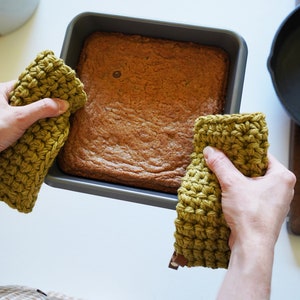 Two hands holding a hot baking dish with pot holders.