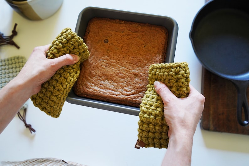 Two hands holding a hot baking dish with pot holders.