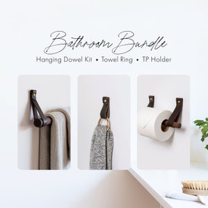 Il kit moderno per il bagno include un porta rotolo di carta igienica da parete in pelle, un portasciugamani da bagno in legno e un piccolo gancio per asciugamani in ottone dorato.