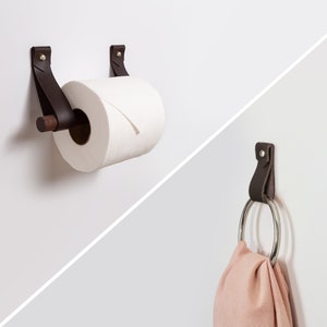 May include: A brown leather toilet roll holder with a wooden dowel and a roll of white toilet paper.  A brown leather hook with a silver ring is also shown.