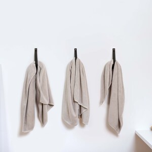Three Large Leather Wall Straps installed on the wall and with a bath towel looped inside the strap.