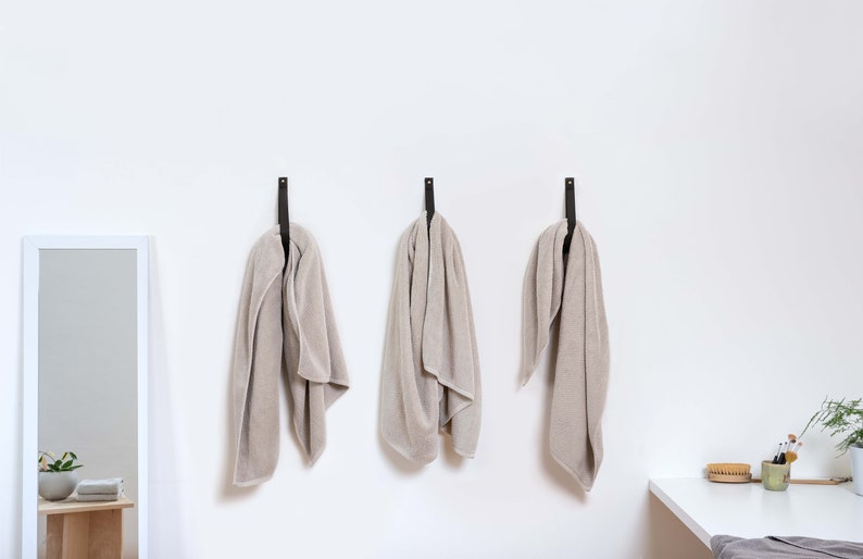 Three Large Leather Wall Straps installed on the wall and with a bath towel looped inside the strap.