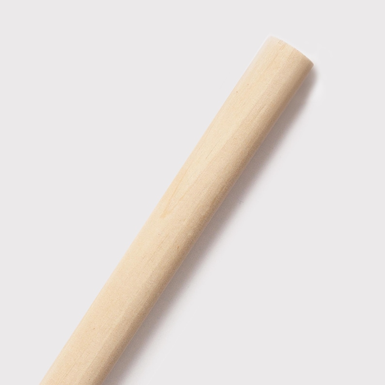 May include: A light-coloured, cylindrical wooden dowel, angled diagonally across the frame. The dowel has a smooth, unfinished surface and a rounded end. The wood grain is visible, and the dowel appears to be new.
