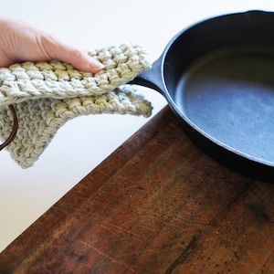 Model holding cast iron pan covering the handle with a pot holder.