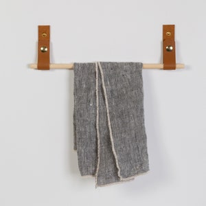 Two wall straps used with a wooden dowel to create a towel bar on which a towel is hung.