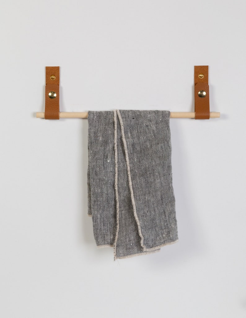 Two wall straps used with a wooden dowel to create a towel bar on which a towel is hung.