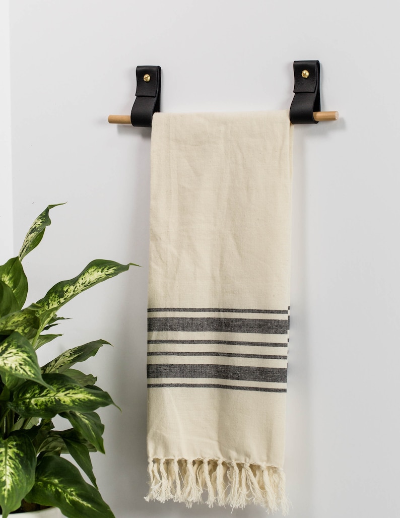 Two wall straps used with a wooden dowel to create a towel bar on which a tea towel is hung.