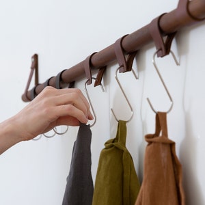 Metal Hooks & Leather Loops hanging from a wooden dowel suspended on the wall.