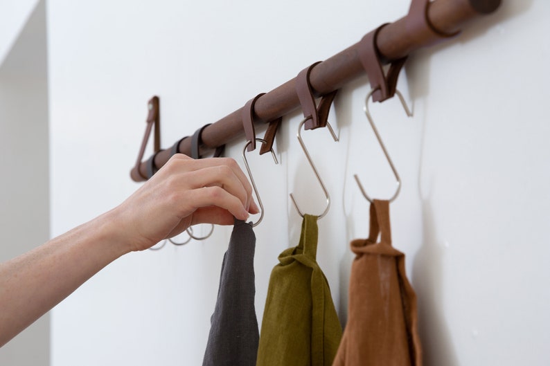 Metal Hooks & Leather Loops hanging from a wooden dowel suspended on the wall.