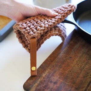 Model holding cast iron pan covering the handle with a pot holder.