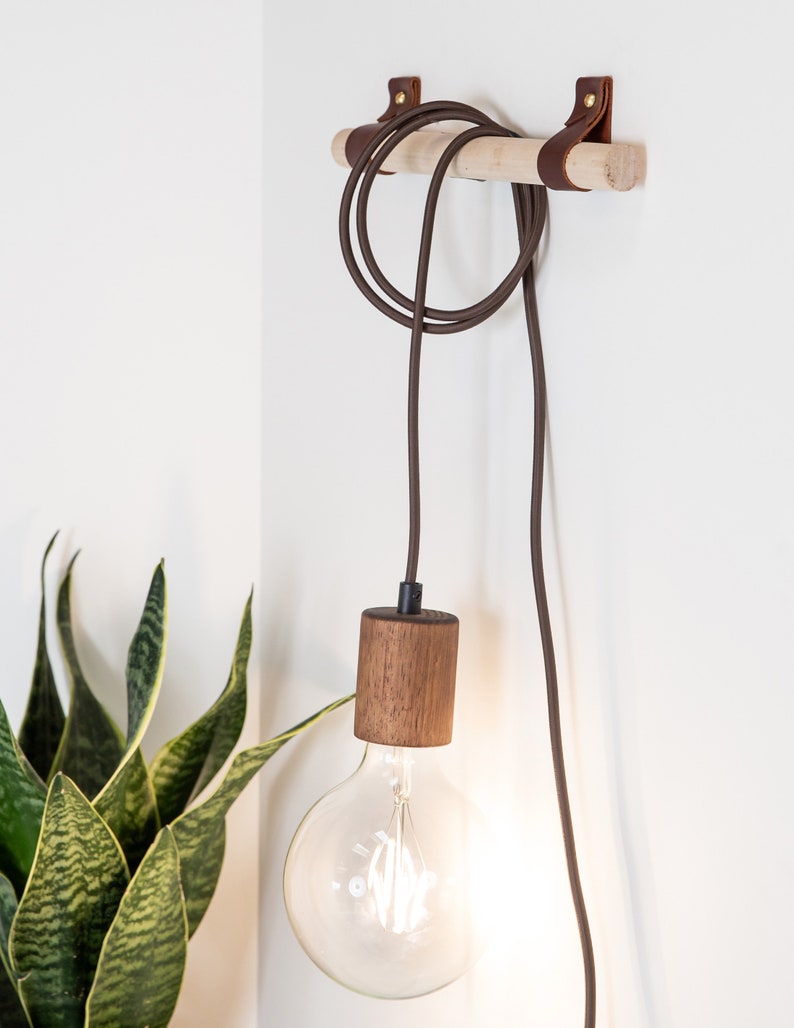 Two wall straps used with a wooden dowel to hang a light cord fixture.