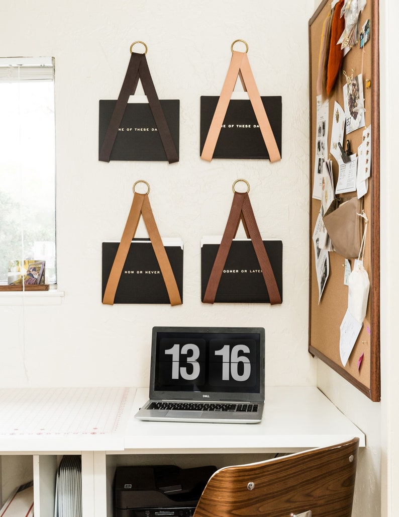 Four File Holders holding black folders on the wall with a cork message board on the right.