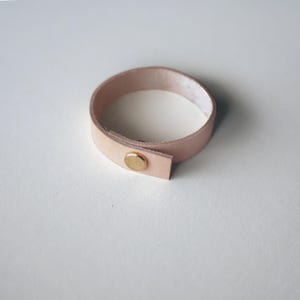 Natural vegetable-tanned leather loop with brass screw closure, showing the pale blush tone of raw leather before patina. Keyaiira's most eco-friendly leather option.