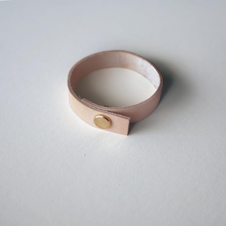 Natural vegetable-tanned leather loop with brass screw closure, showing the pale blush tone of raw leather before patina. Keyaiira's most eco-friendly leather option.