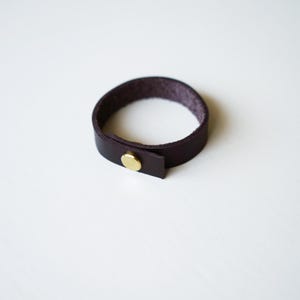Rich dark chocolate brown colored leather - full-grain leather loop with subtle texture and brass hardware, photographed on a white surface.