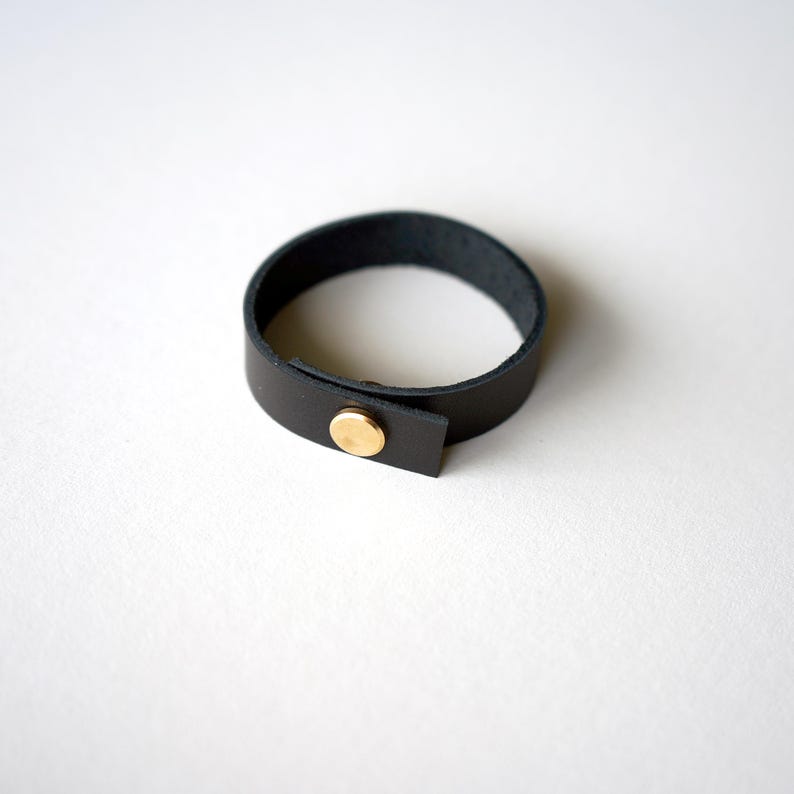 Modern black full-grain leather loop with a polished brass screw closure, shown on a clean white background.