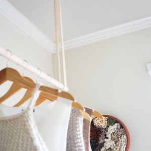 A closeup of Leather Suspension Straps and a wooden dowel used for a Garment Rack in the corner of a bedroom.