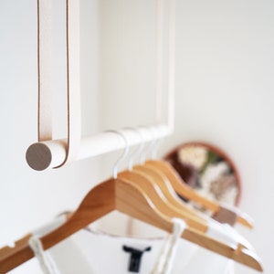 A closeup of Leather Suspension Straps and a wooden dowel used for a Garment Rack in the corner of a bedroom.