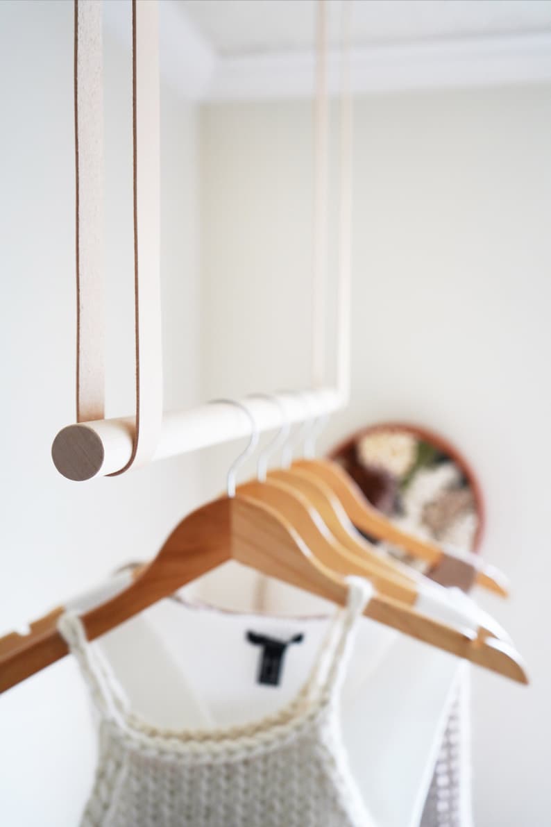 A closeup of Leather Suspension Straps and a wooden dowel used for a Garment Rack in the corner of a bedroom.