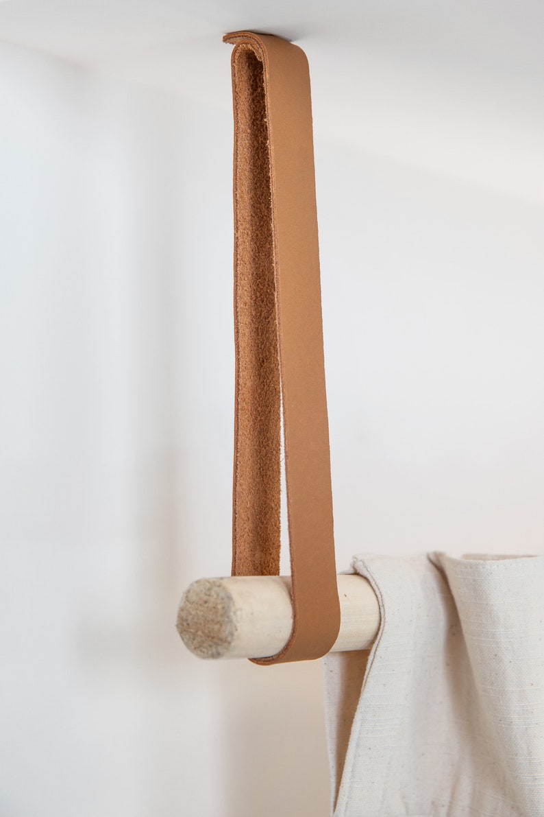 A closeup of a Leather Suspension Strap hanging a curtain with a wooden dowel.